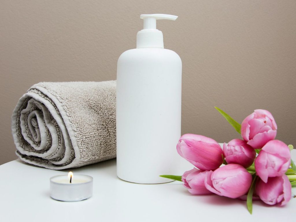 towel, scented candle, flowers and cream bottle on a table