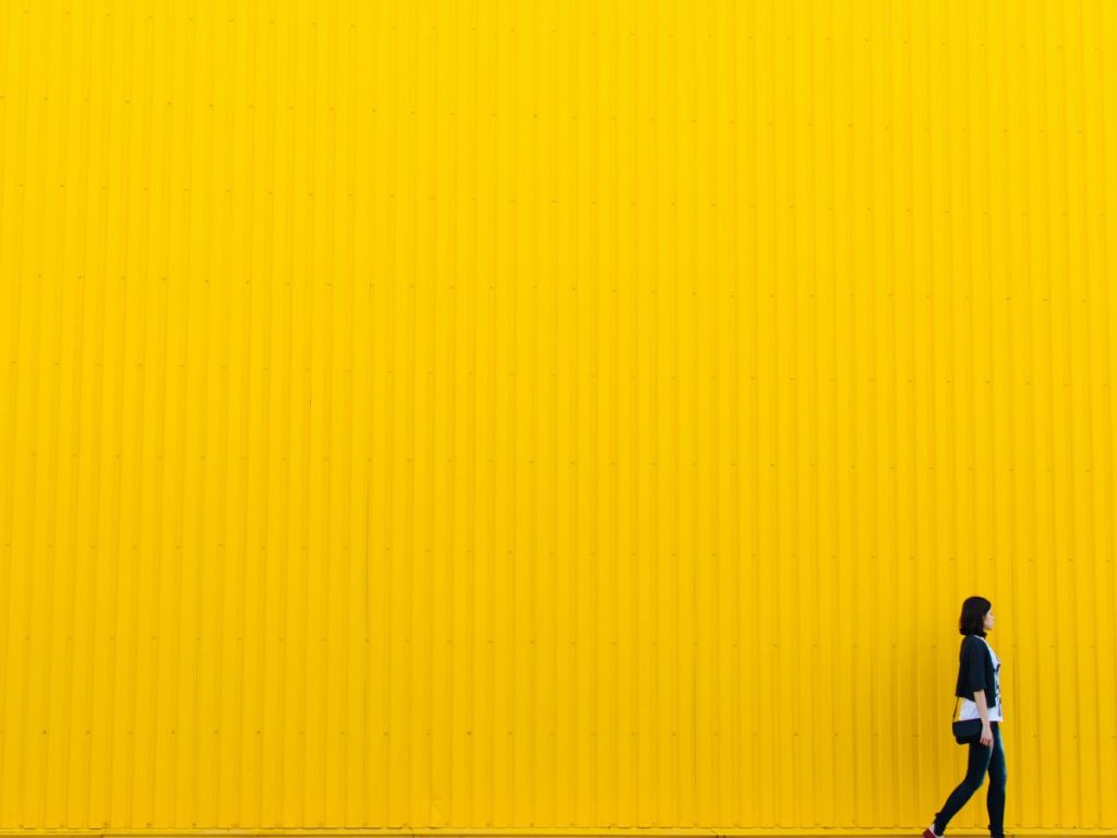 Girl walking over yellow wall